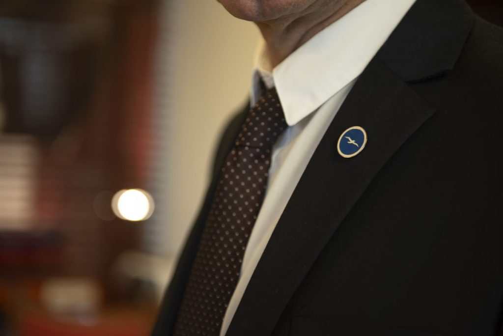 man in a suit with a pin with Piraeus Marine Club logo