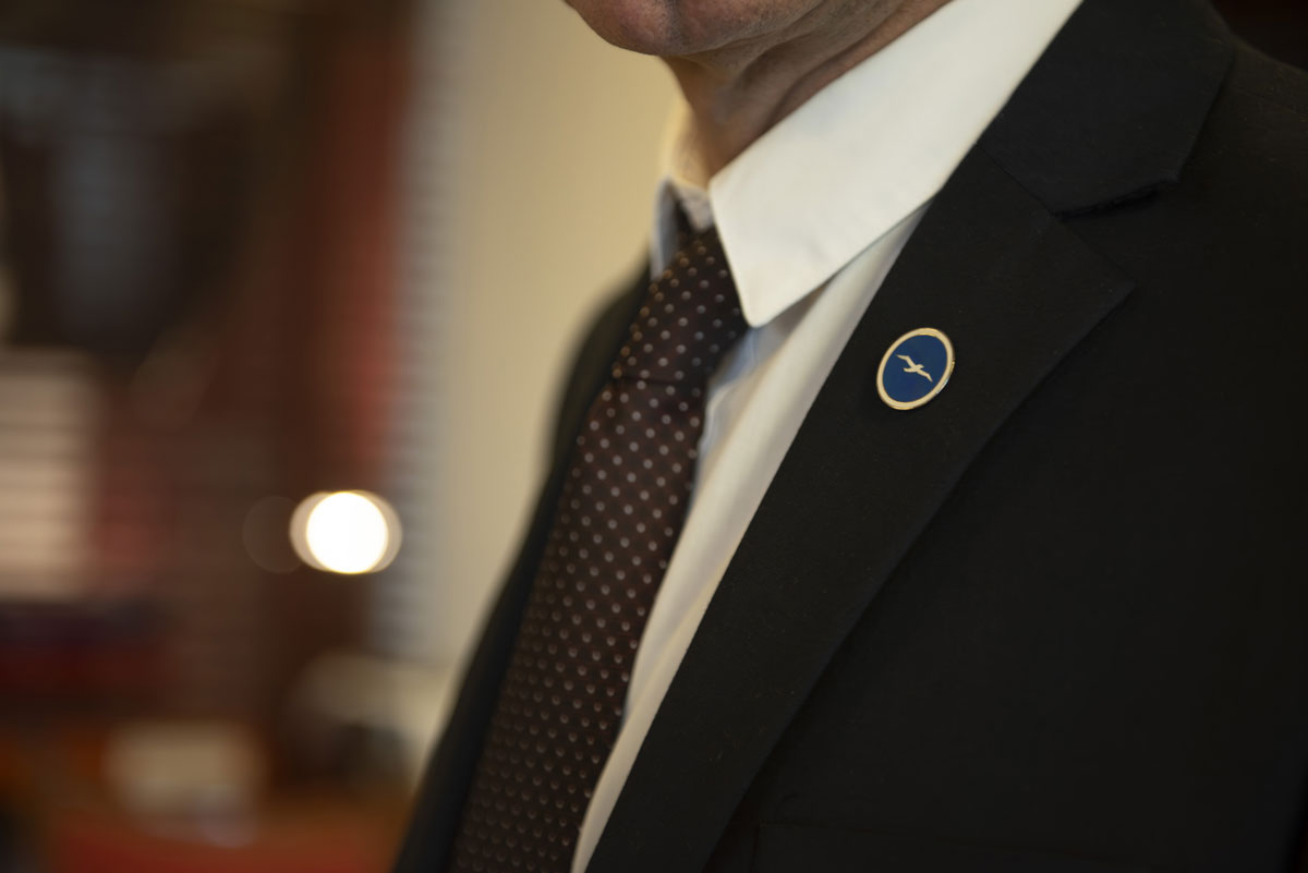 man in a suit with a pin with Piraeus Marine Club logo